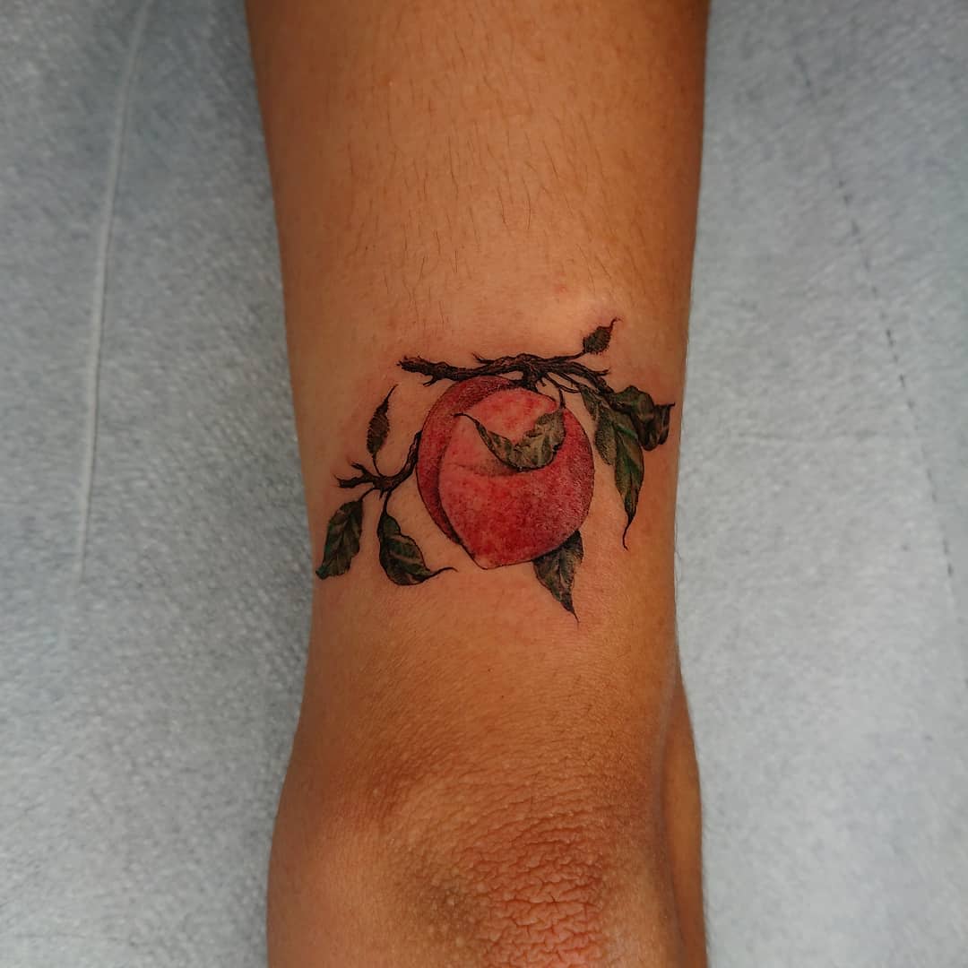 Tattoo of a peach with leaves and branches on a forearm